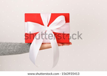 Closeup of a box with a gift and a bow on a female hand on a light wall background.