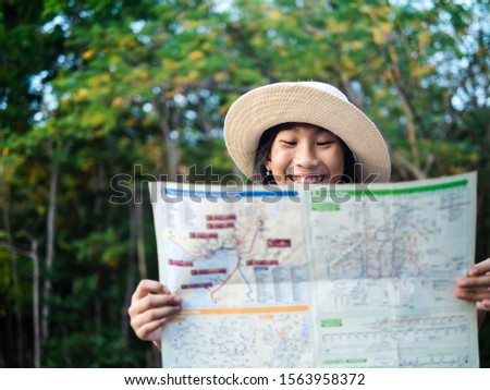 Young girl reading map with tree background, lifestyle concept.