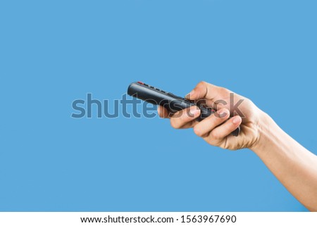 man's hand holding a TV remote control isolated on a light blue background 
 Royalty-Free Stock Photo #1563967690