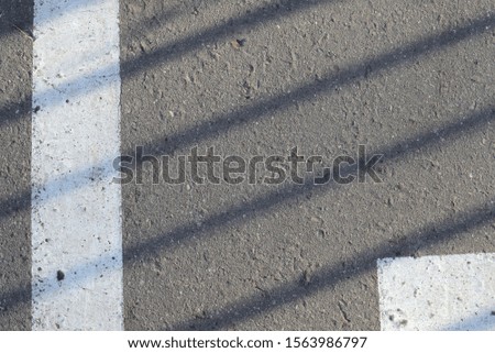 Closeup of asphalt surface with white paint and shadow from the fence on it. Abstract background