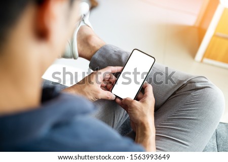 Mockup image blank white screen cell phone.men hand holding texting using mobile relax on sofa at home. background empty space for advertise text.people contact marketing business and technology  Royalty-Free Stock Photo #1563993649