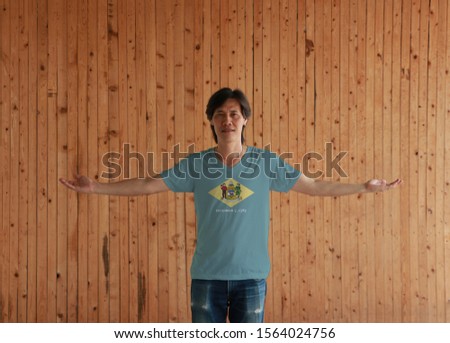 Man wearing Delaware flag shirt and standing with arms wide open on the wooden wall background, the states of America. 