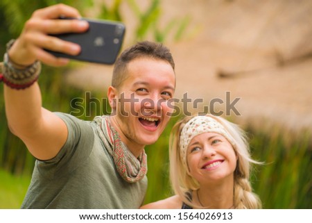 young happy and beautiful hipster couple taking selfie picture with mobile phone outdoors enjoying holiday at tropical nature background smiling and  exploring exotic tourist destination
