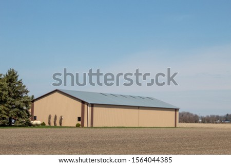 A large farm building next to a corn field.
