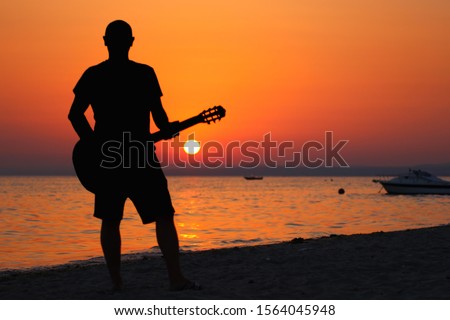 Man with guitar in hands at sunset