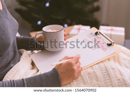 Woman creating her Christmas wish list for Santa, home interior, blurred background, copy space