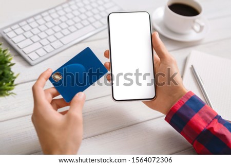 Online payment. Man holding smartphone with blank screen and credit card, making financial transaction