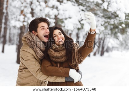 Christmas Mood. Happy Couple Taking Selfie On Cellphone Smiling And Hugging Standing In Winter Forest