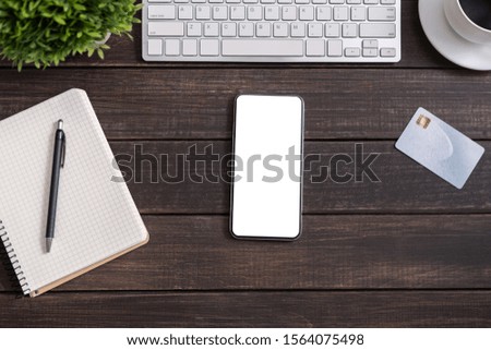 Modern smartphone with white blank screen on wooden office table, top view