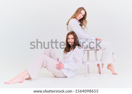 two girls in white clothes pose with a chair on a white background in a photo Studio