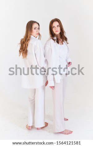 two girls pose in white clothes on a white background in a photo Studio