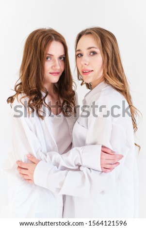 two girls in white clothes embrace on a white background in a photo Studio
