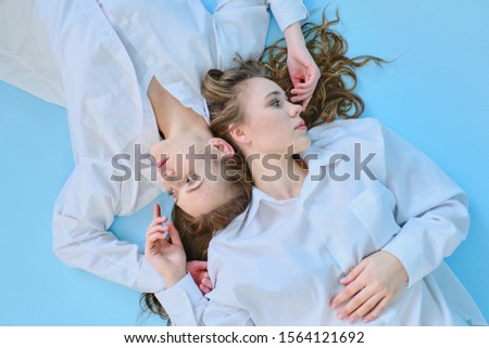 two girls in white clothes pose against a blue background in a photo Studio top view