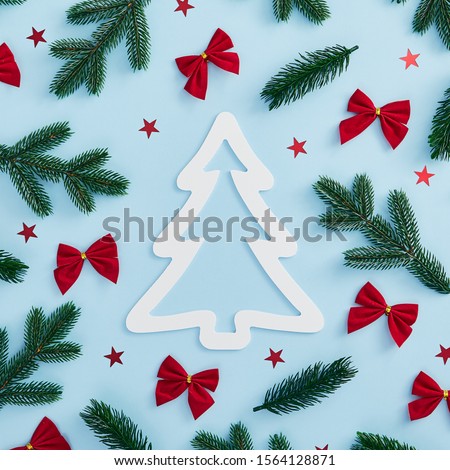 Christmas minimal concept - Christmas tree branch, confetti star and red bow decoration on blue background. Square template. White paper xmas tree shape. Christmas greeting card design template.