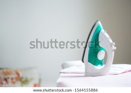 cordless iron on a pink ironing board next to a folded shirt  Royalty-Free Stock Photo #1564155886