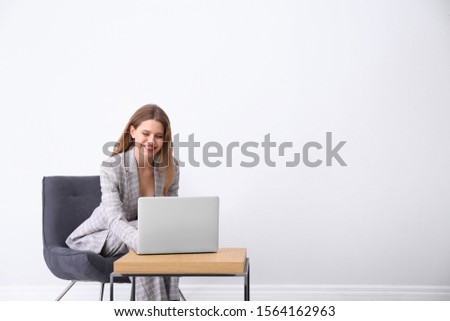 Young woman working with laptop in armchair indoors. Space for text