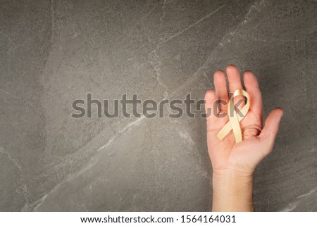 golden ribbon childhood symbol of the fight against cancer in male hands on a gray background. concept of helping patients with sarcoma and bladder cancer.