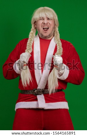 Male actor dressed as Santa Claus with long braid hairstyle grimaces and poses on a green chroma background