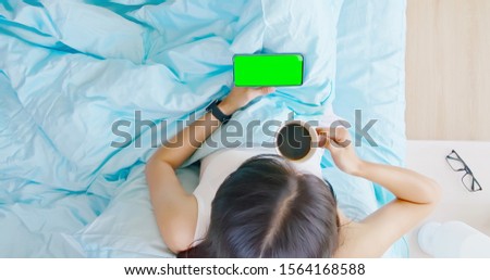 overlooking of asian woman use smartphone with green screen on the bed and drink coffee in the room