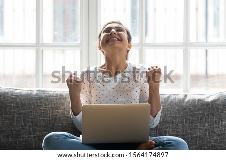 Overjoyed young indian woman celebrating personal achievement, sitting with computer on couch at home. Happy euphoric millennial girl getting grant university scholarship or employment notification. Royalty-Free Stock Photo #1564174897