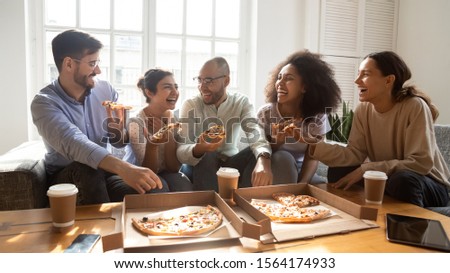 Overjoyed young diverse buddies eating ordered pizza for home party. Happy mixed race young friends enjoying spending free weekend time together, laughing, joking, communicating, having fun. Royalty-Free Stock Photo #1564174933