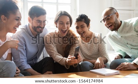 Overjoyed young mixed race friends watching funny video content on smartphone. Happy excited multiracial people having fun at home. Crazy millennial diverse classmates enjoying spending time together. Royalty-Free Stock Photo #1564174984