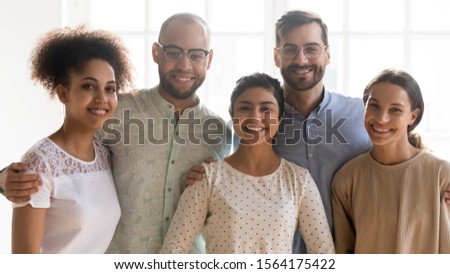 Head shot portrait of happy diverse friends, embracing near window. Smiling group of mixed race young students, positive multiracial colleagues team looking at camera, posing for photo together.