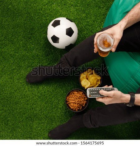 A man sits at the TV and watches a football match. Sneki TV remote. Soccer ball. View from above. Copy space.