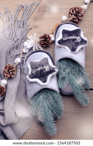 Gray soft home slippers and Christmas decor on a brown wooden background. Cozy.