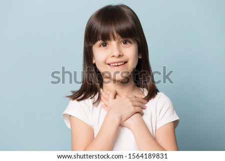 Close up head shot portrait image with smiling and cute little brown-haired girl. Concept happy kid lovely hold abstract heart on blue background, six year child looking at camera and gesture