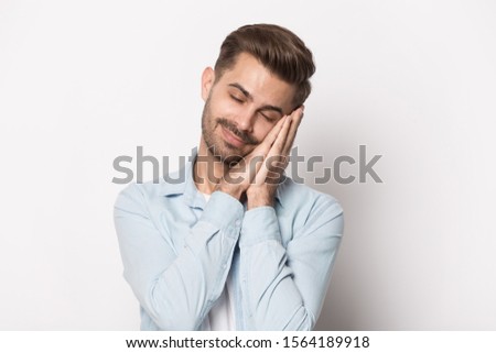 Close up head shot image of happy asleep handsome bearded man. Young smiling calm student standing sleeping with head on hands eyes closed isolated on grey background, healthy peaceful sleep concept