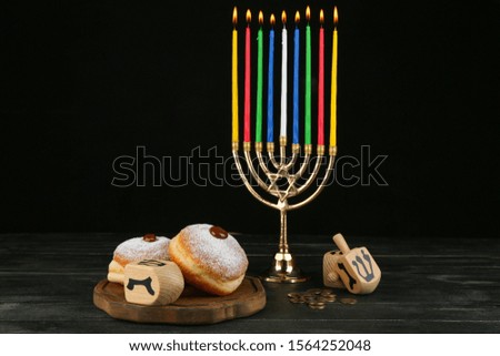 Menorah, donuts for Hanukkah and dreidels on table against dark background