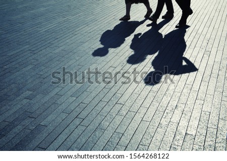 Morning sun casting dramatic shadows on a plaza behind silhouettes of commuting business people rushing to work