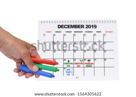 December 2019 Calendar with Christmas Eve, Christmas, Kwanzaa and New Years Eve Hand holding red, blue and green crayon white background