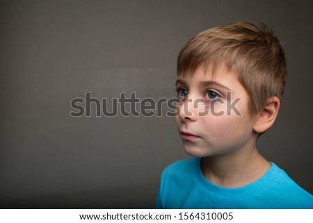 portrait of a boy of 7 years old, blue - green eyes. child is wearing a blue t-shirt on a gray background, smiling Royalty-Free Stock Photo #1564310005
