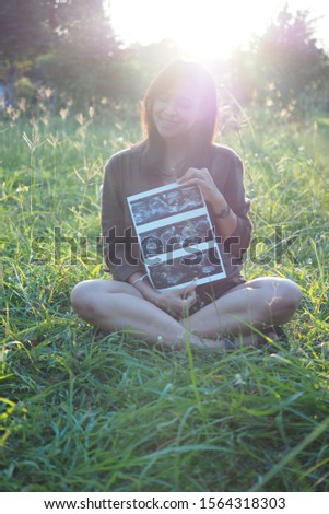 Silhouette of asian pregnant girl sit on the yard and hold pregnancy ultrasound
picture front of her face. Happy pregnancy concept.