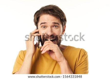 A man in a yellow T-shirt covers his mouth with his hand and holds the phone near his ear