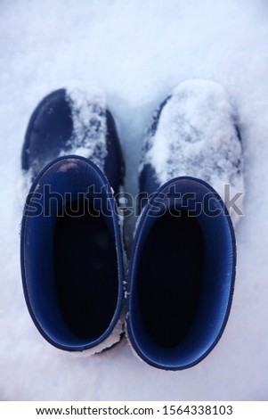 Blue pair of wellies in snow. Close up. Ready for winter. Focus on the top of the wellies. A similar picture is available where the focus is on the lower part of the wellies and the snow.