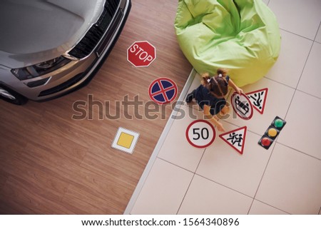 Top view of cute little girl that paint road signs on the floor near the modern car.