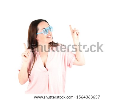 Excited young woman looking and pointing up while wearing blue sunglasses against a white background