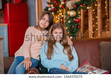 two friends - girls sitting on the couch - posing in the Christmas decorated wooden house - school aged girls