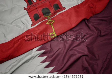 waving colorful flag of qatar and national flag of gibraltar. macro