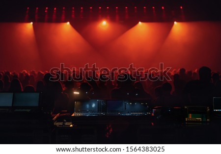 Concert crowd in music hall. Stage lighting equipment and bright red projector lights on rave party in night club. Electronic music festival background