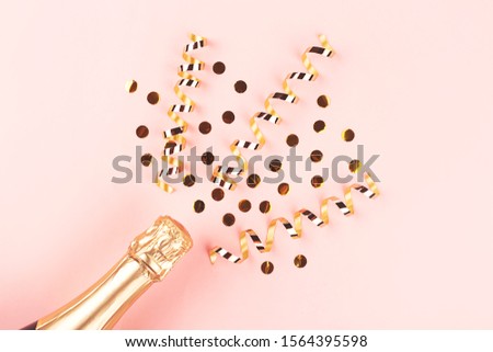 Creative New Year composition with champagne bottle and exploding gold confetti and streamers. Celebration and party concept.