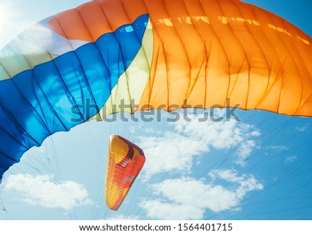 Colorful Paraglider waving on the wind with sunbeams optical flares with blu sky background. Active people concept image.
