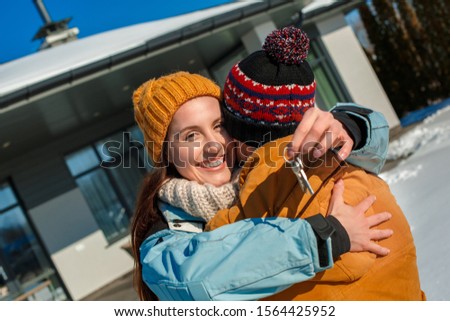 Young couple on a winter vacation spending time together outdoors standing holding keys from new apartment looking camera smiling happy
