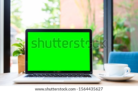 Mockup of laptop computer with empty screen with coffee cup on table of the coffee shop background,green screen