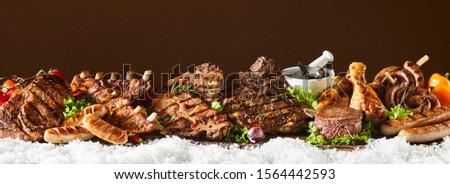Panorama banner with large selection of barbecued meat including sausage, beef, pork, spare ribs, chicken on a bed of salad greens on winter snow with copy space