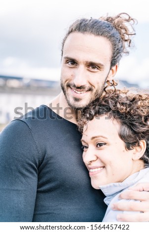 Stock vertical photo of a couple embraced by the shoulder with the sea out of focus in the background. Lifestyle