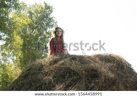 Blonde girl near a haystack. A wreath of flowers on the head. haymaking.